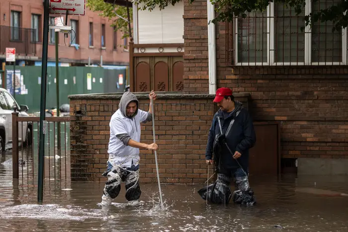 Two men try to clean up sewage in Brooklyn following a storm.